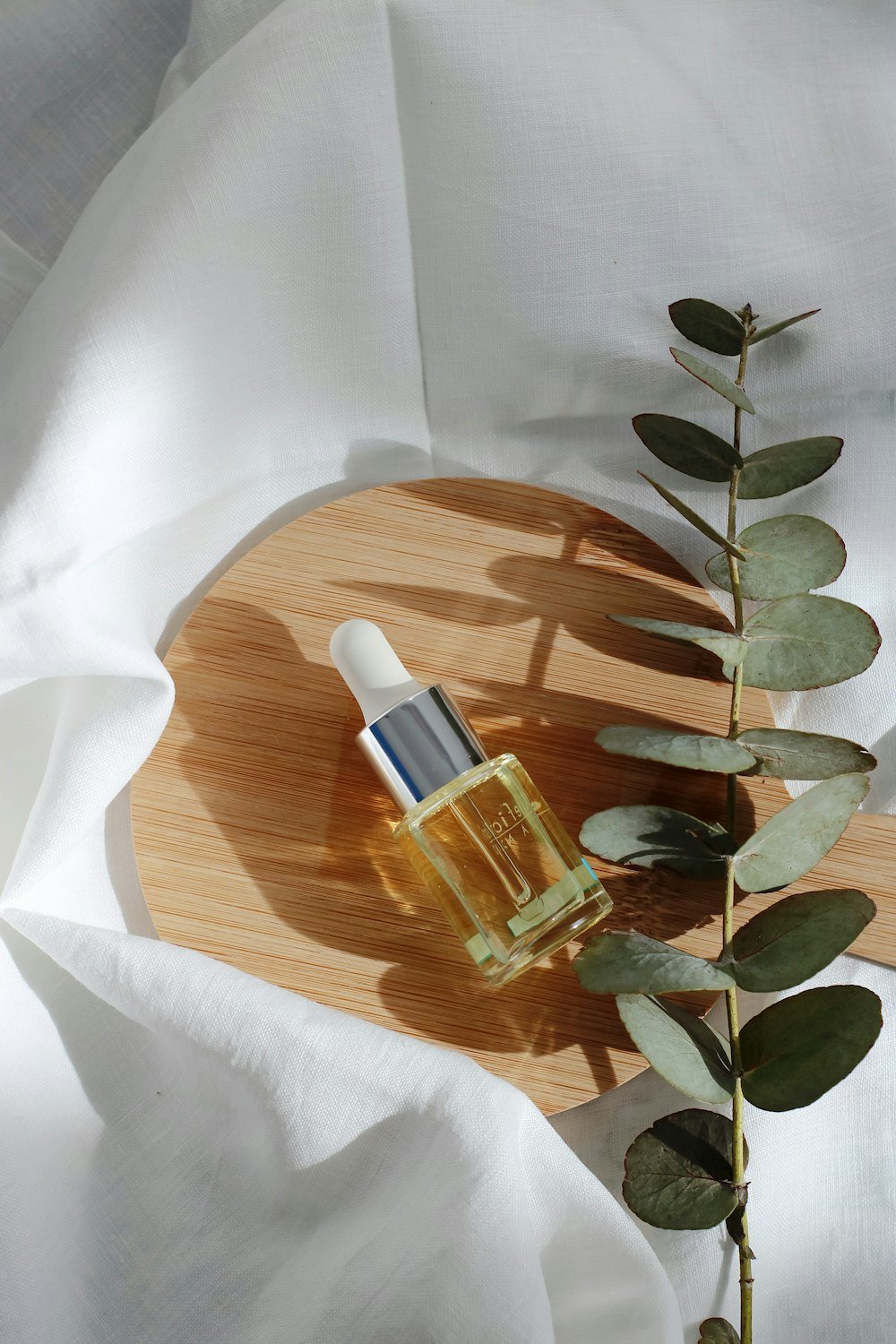 Golden facial serum bottle with eucalyptus on a wooden tray at Bloom